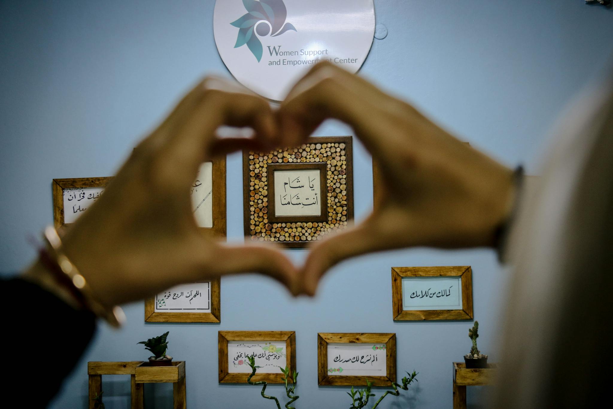 Hands forming a heart shape framing Arabic script art on a wall at a women's center.